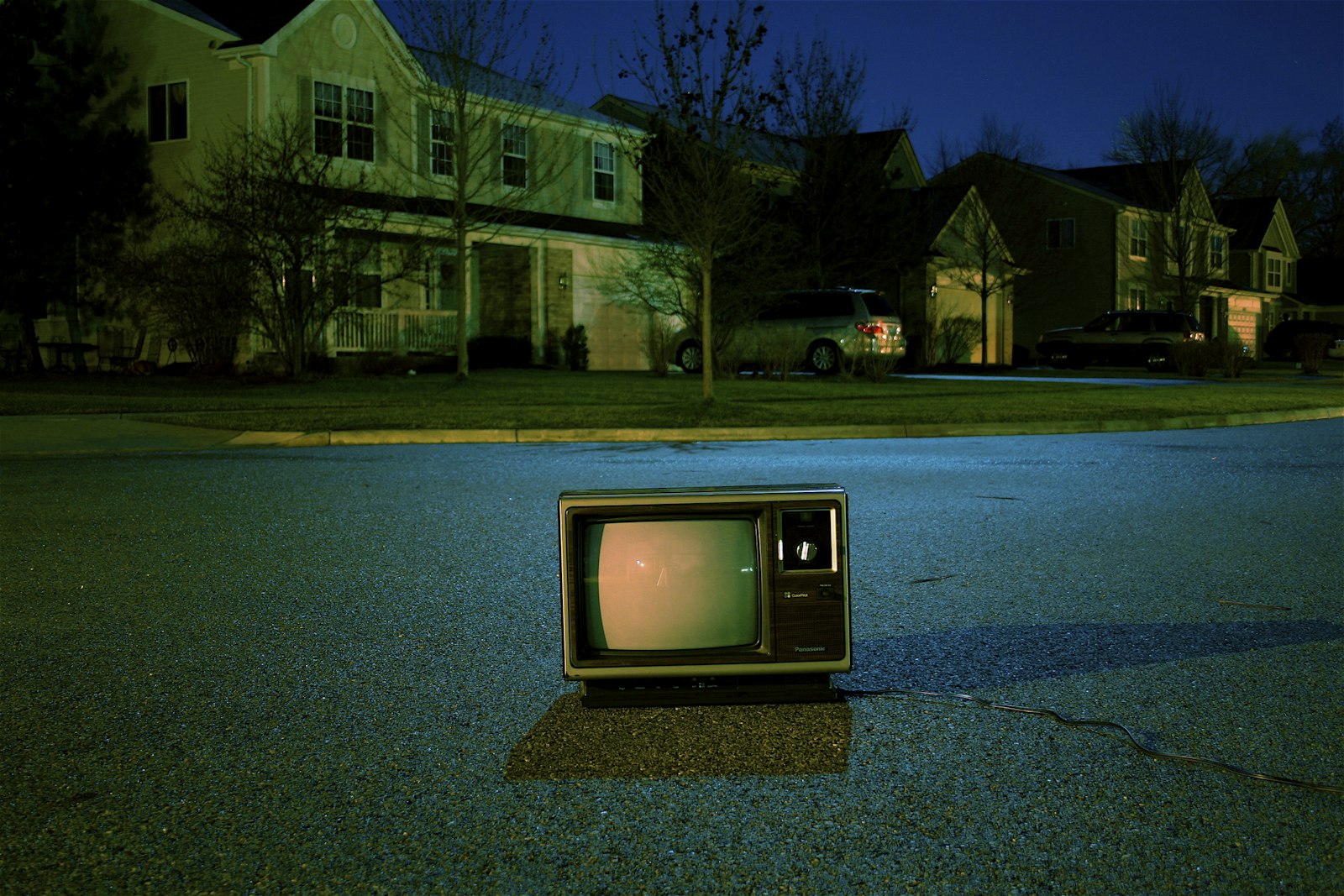 A vintage television set sitting alone on a quiet suburban street at dusk